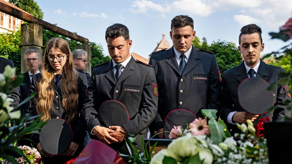 Mannheim: Drei Männer und eine Frau stehen vor Blumen und halten ihre Köpfe zum Gedenken gesenkt.
