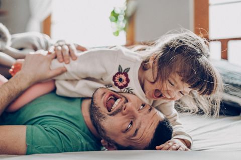 Vater tobt mit seiner kleinen Tochter lachend auf dem Bett