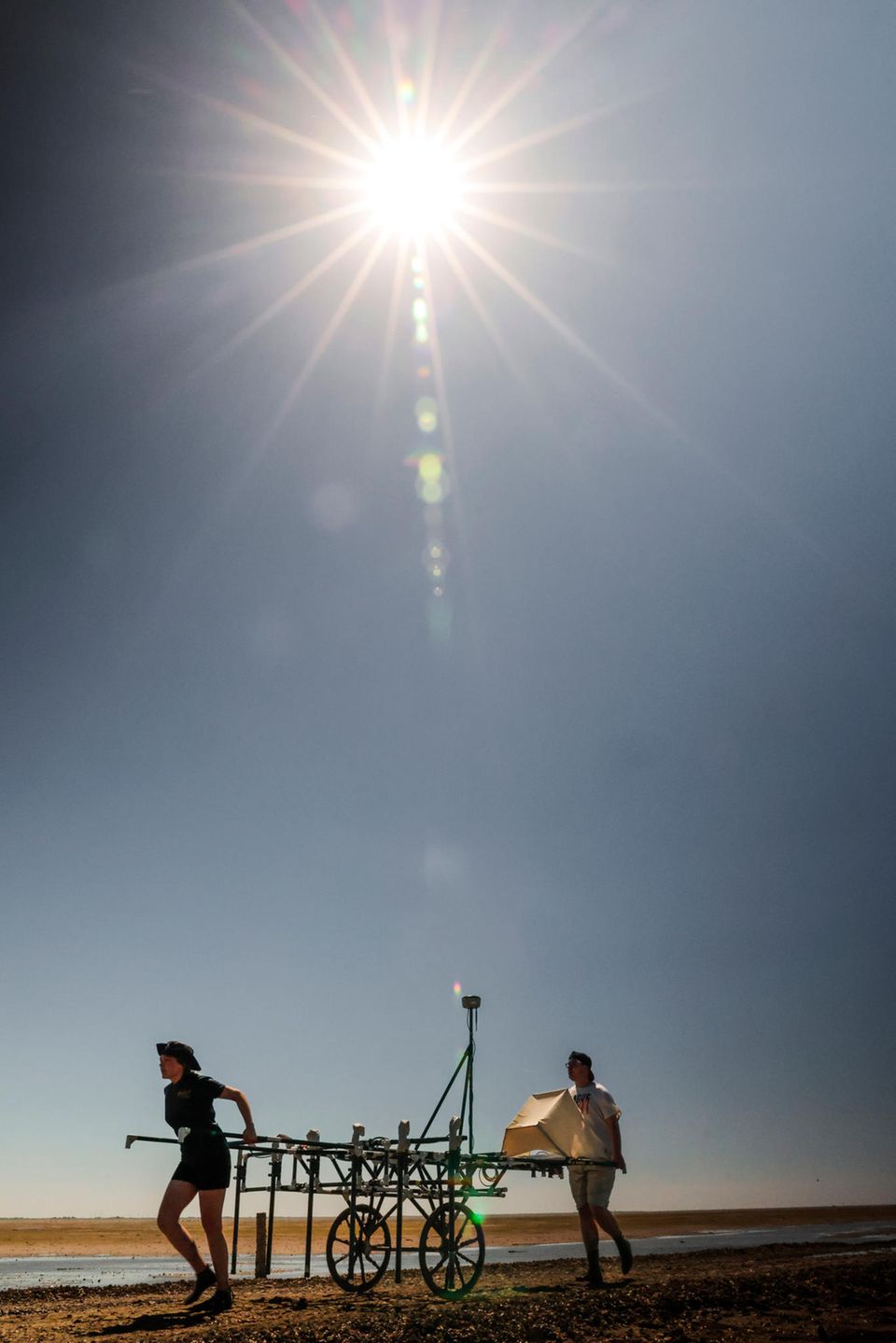Studierende schieben einen Magnetikwagen durchs Watt, die Sonne knallt vom Himmel auf die beiden