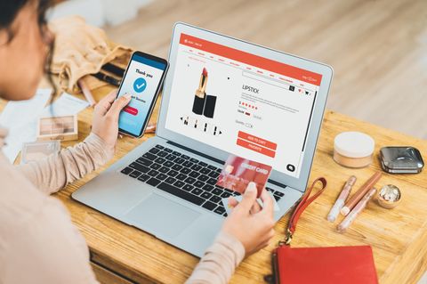 Symbolbild Schuldnerberatung: Eine Frau sitzt vor einem Laptop und kauft mit einer Kreditkarte Lippenstift