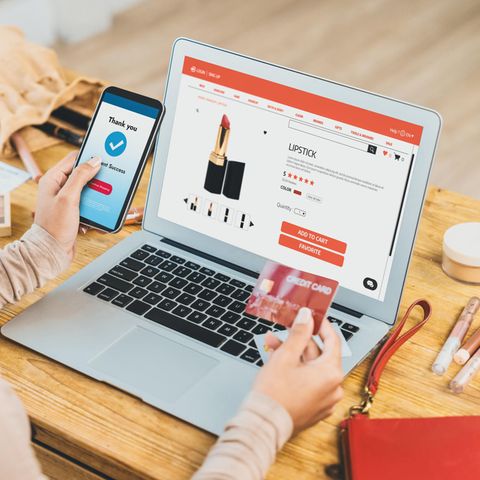 Symbolic image of debt advice: A woman sits in front of a laptop and buys lipstick with a credit card