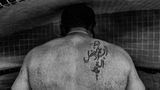 Shahram in einem Bad, fotografiert von hinten, man sieht eine Tätowierung auf der rechten Schulter