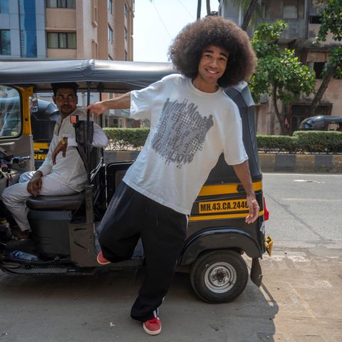 Influencer und Tiktok-Star Noel Robinson steigt aus einer Rikscha auf die Straße, er hat eine Afro und trägt ein weißes Shirt