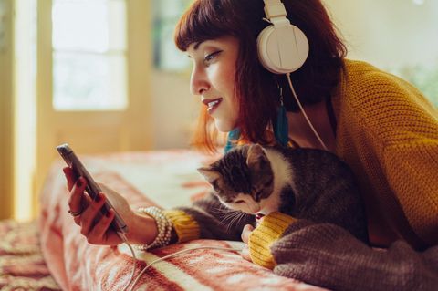 Smartphone-Tarife für junge Leute – junge Frau mit Katze und Handy auf dem Bett.