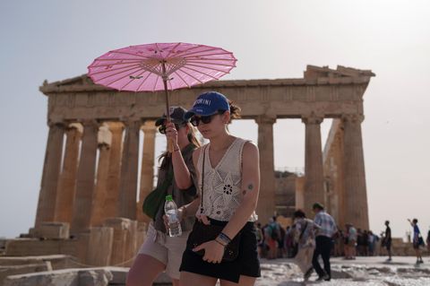 Touristen gehen mit einem Schirm vor dem Parthenon spazieren