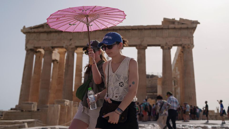 Touristen gehen mit einem Schirm vor dem Parthenon spazieren