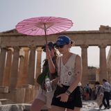Touristen gehen mit einem Schirm vor dem Parthenon spazieren