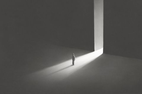 Eine Person steht vor zwei hohen Wänden, durch die Lücke zwischen ihnen fällt Licht