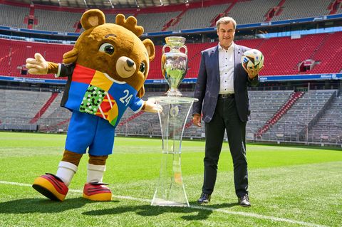 Markus Söder steht neben dem Fußball-EM Maskottchen und dem EM Pokal im Stadion