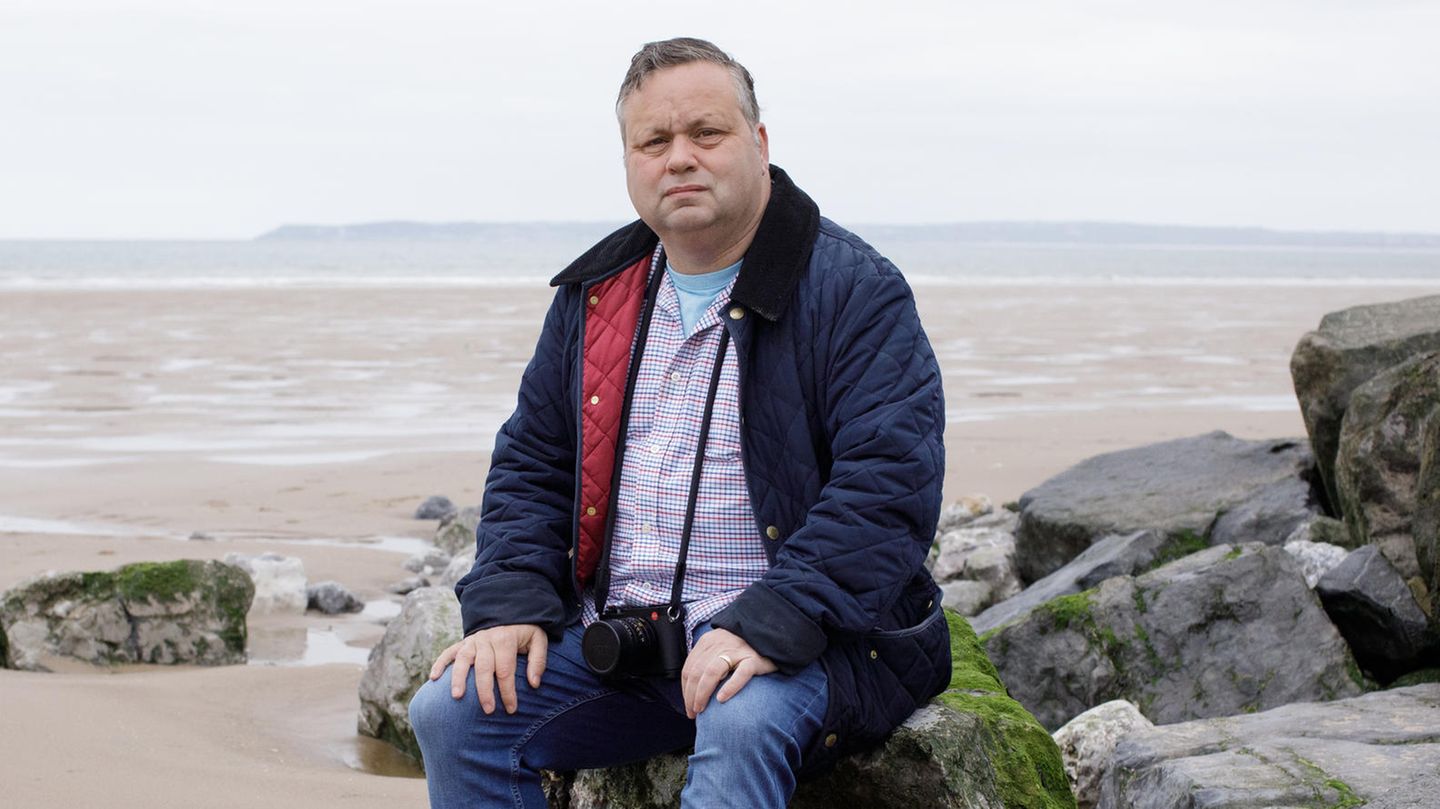 Paul Potts sitzt auf einem Stein am Meer
