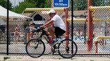 Ein Mann fährt bei heißem Wetter mit dem Fahrrad auf den Woodland Trails des River Trails Park District in Mount Prospect, Illinois. Im Hintergrund vergnügen sich Kinder lieber auf einem Wasserspielplatz