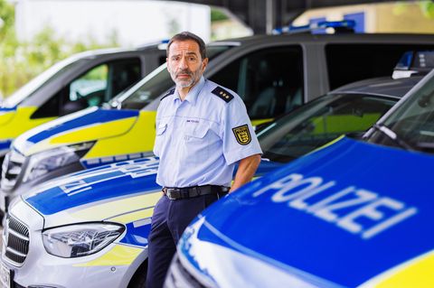 Portrait eine Polizisten zwischen Polizeiautos