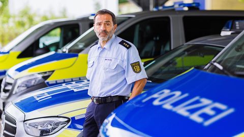 Portrait eine Polizisten zwischen Polizeiautos