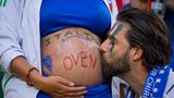 Ein Mann küsst den Babybauch einer Schwangeren, auf den italienische Fansprüche gemalt sind