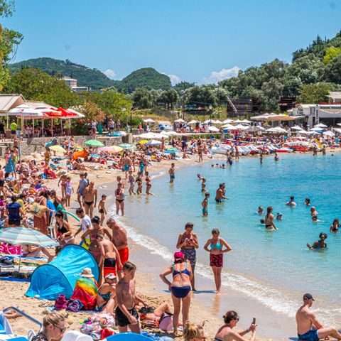 Pauschalreisen sind beliebt: Menschen am Strand und Boot in Paleokastrttsa, Korfu