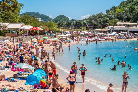 Pauschalreisen sind beliebt: Menschen am Strand und Boot in Paleokastrttsa, Korfu