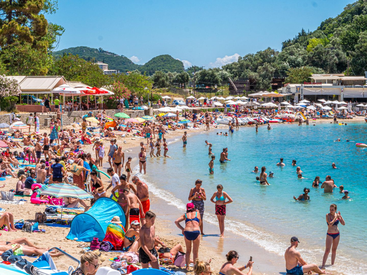 Pauschalreisen sind beliebt: Menschen am Strand und Boot in Paleokastrttsa, Korfu