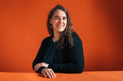 Heike Heubach sitzt an einem Tisch und lächelt in die Kamera. Sie trägt die langen Haare offen und Ohrringe.