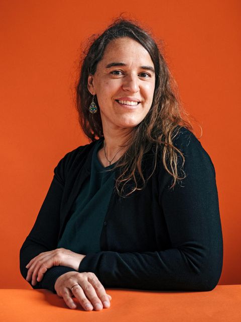 Heike Heubach sitzt an einem Tisch und lächelt in die Kamera. Sie trägt die langen Haare offen und Ohrringe.