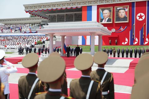 Die beiden Machthaber verfolgen das Spektakel im Schatten eines Unterstands mit antiker Anmutung. Im Hintergrund hängen übergroße Porträtbilder von Kim und Putin. Die Bildsprache spricht Bände