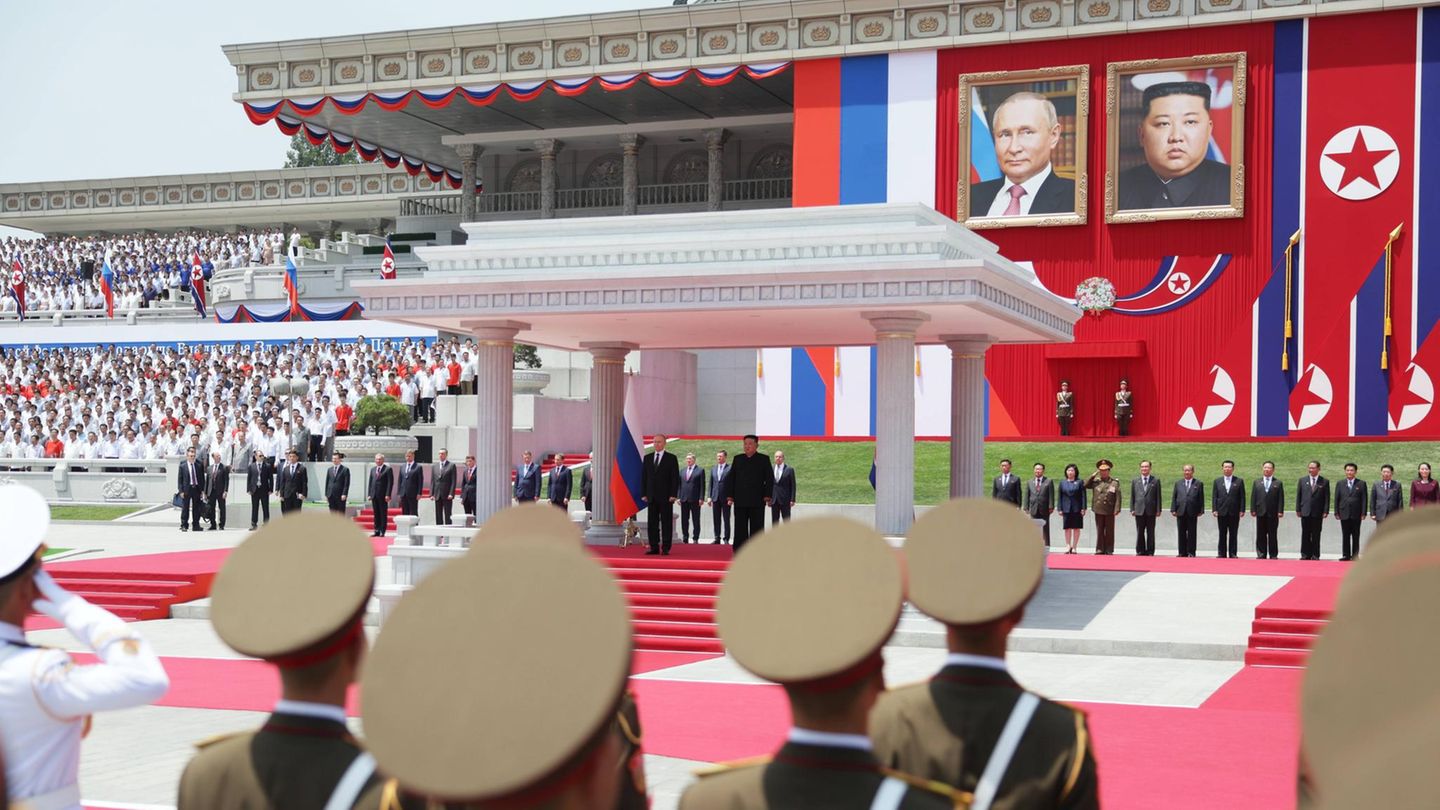Die beiden Machthaber verfolgen das Spektakel im Schatten eines Unterstands mit antiker Anmutung. Im Hintergrund hängen übergroße Porträtbilder von Kim und Putin. Die Bildsprache spricht Bände