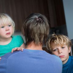 zwei Kinder schauen ber den Rücken eines Elternteiles.