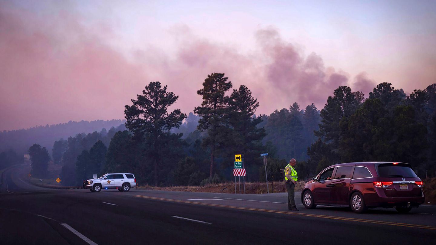 Der Rauch des South Fork Fire spiegelt bei Sonnenaufgang einen rosafarbenen Farbton wider, als Polizisten Autofahrer auf der State Road 48 an der State 220 wegen der Waldbrände in der Nähe von Ruidoso, New Mexico, anhalten