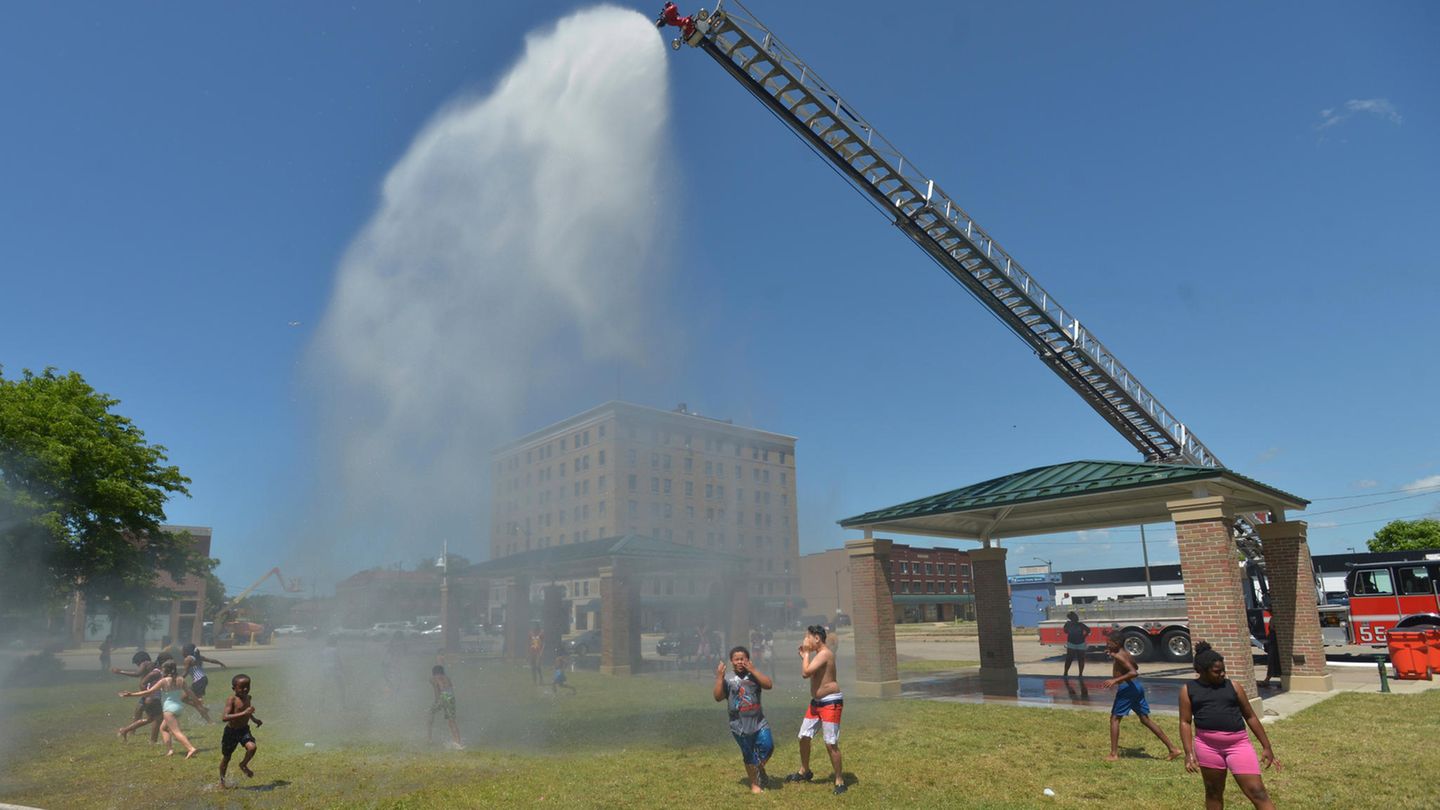 Kinder erfrischen sich unter dem Wasserstrahl, der von einem Leiterwagen auf einen Park in Benton Benton Harbor, Michigan, niedergeht