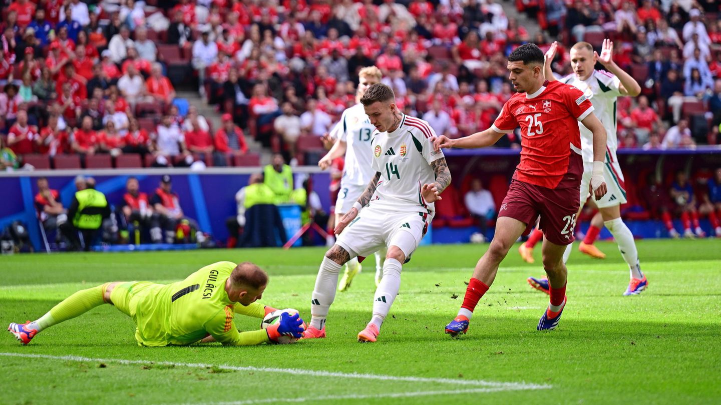Torwart hält liegend ausgestreckt den Ball fest, während zwei Spieler vor ihm stoppen