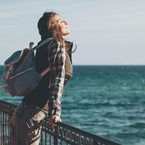 Eine Frau an einer Promenade am Meer schließt genüsslich die Augen