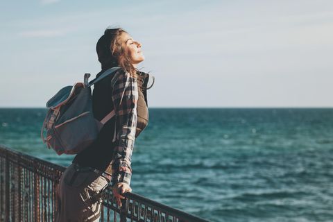 Eine Frau an einer Promenade am Meer schließt genüsslich die Augen