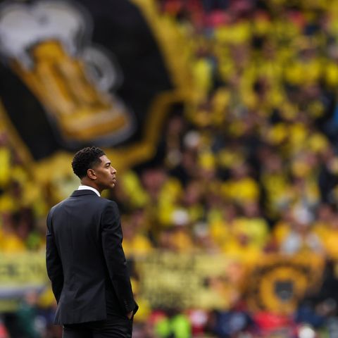 ein Mann im schwarzen Anzug steht auf einem  Fussballrasen