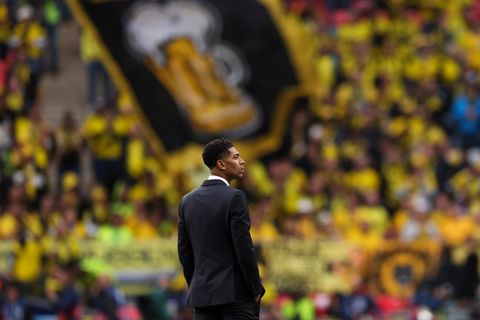 ein Mann im schwarzen Anzug steht auf einem  Fussballrasen