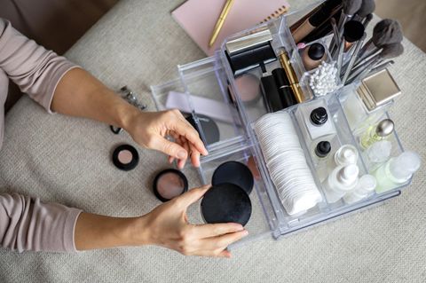 Jemand sortiert Kosemtik in einen Make-up-Organizer.