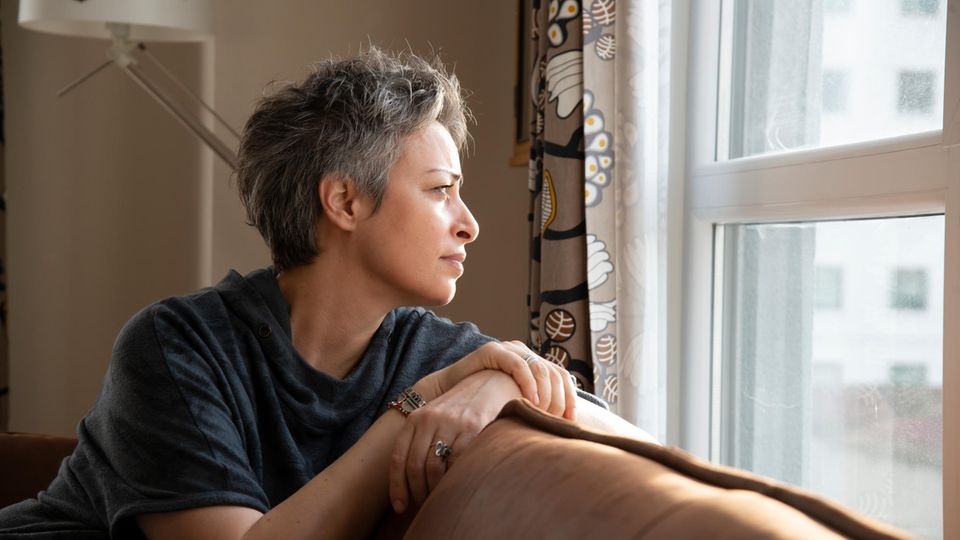 Eine Frau mittleren Alters sitzt auf einem Sofa und schaut auf dem Fenster.