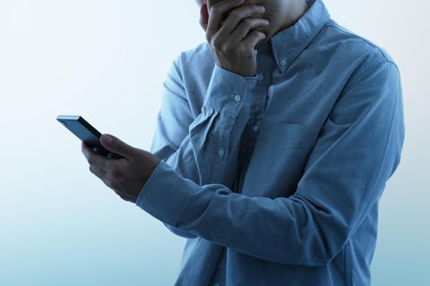 Smartphone gehackt: Mann mit Smartphone in der einen Hand, die andere Hand vor dem Mund.