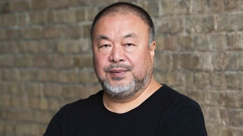 Künstler Ai Weiwei in einem schwarzen T-Shirt vor einer Backsteinwand