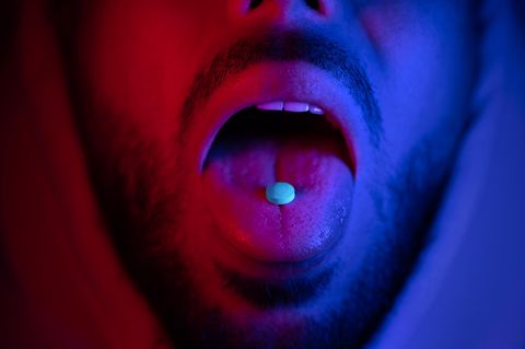 Nahaufnahme des Mundes des Mannes, der Ecstasy-Drogen schluckt (Symbolbild)