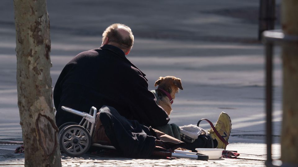 Ein Mann sitzt mit seinem Hund an der Straße und wartet auf Gaben von Passanten