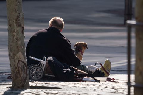 Ein Mann sitzt mit seinem Hund an der Straße und wartet auf Gaben von Passanten