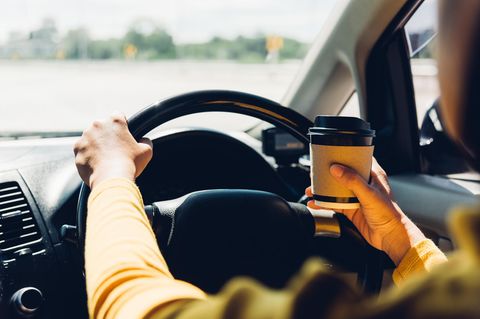 Getränkehalter im Auto: Frau mit Kaffeebecher am Steuer eines Autos