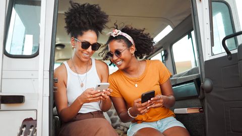 iPhone-Vergleich: Zwei Frauen sitzen lachend mit Smartphones in einem Camper.