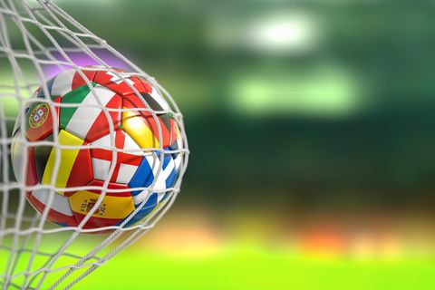 Ein Fußball, geschmückt mit den Landesflaggen der EM-Teilnehmer, fliegt ins Tornetz