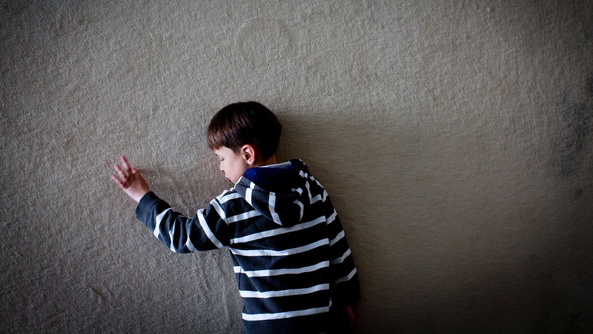Völlig versunken fährt Jasper mit seinen Fingern die linien einer Teppichwand in der Rehaklinik nach