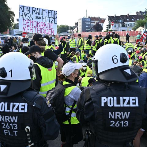 Demonstranten stehen und sitzen auf einer Zufahrtsstraße zum Gelände des AFD-Parteitags – einige halten ein Schild mit der Aufschrift "Kein Raum für Hass und Hetze – Demokratie verteidigen"