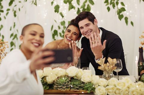 Fotoaufgaben Hochzeit: Eine Frau macht ein Selfie mit dem Brautpaar.