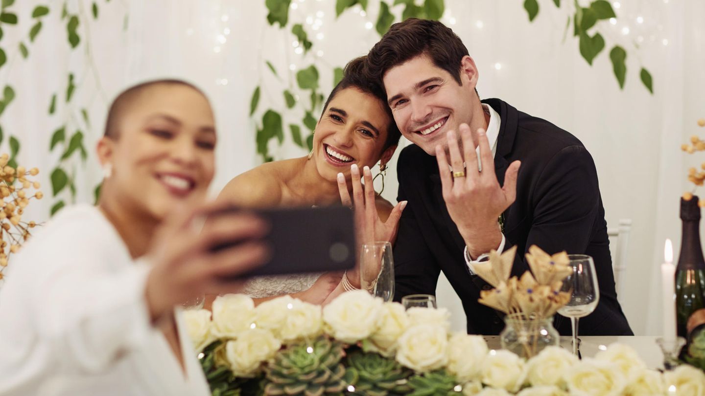 Fotoaufgaben Hochzeit: Eine Frau macht ein Selfie mit dem Brautpaar.