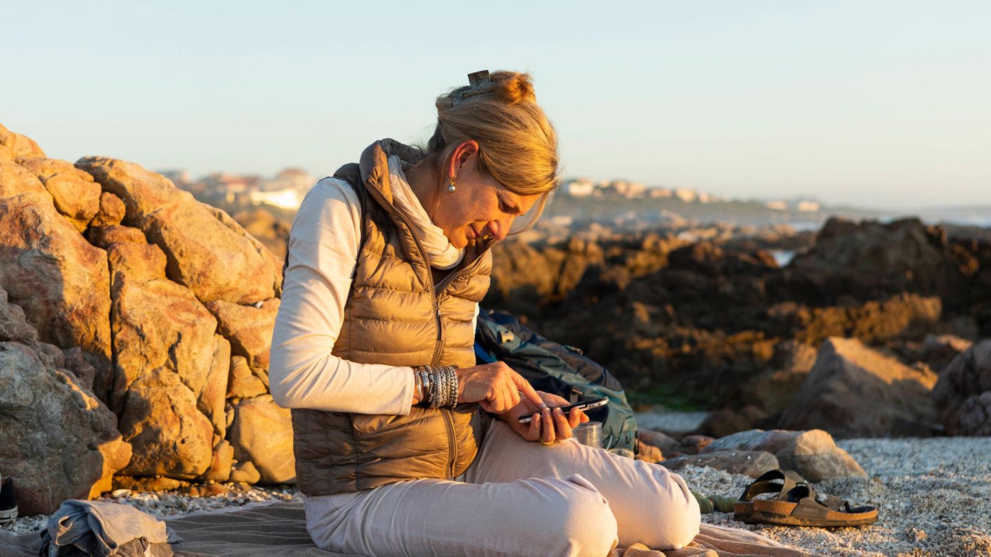 Urlaub: Frau am Strand checkt ihr Smartphone