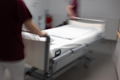 Eine Krankenpflegerin und ein Krankenpfleger schieben ein Krankenbett durch den Gang einer Station eines Krankenhauses