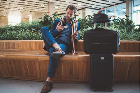 Amex-Punkte in Meilen umwandeln - Mann sitzt mit Koffer und Kreditkarte in der Hand am Flughafen.